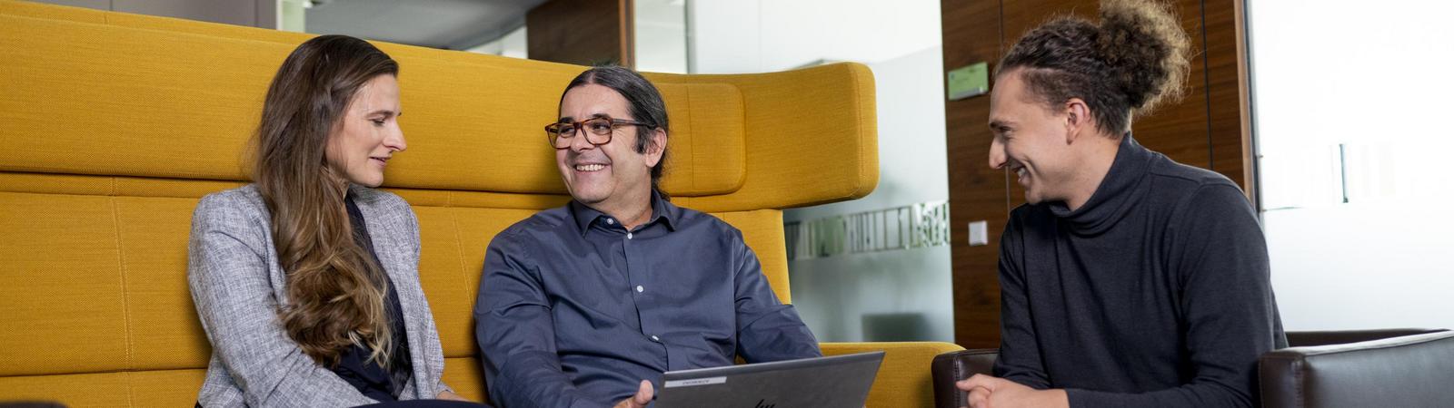 3 Kolleg:innen arbeiten auf Notebook zusammen