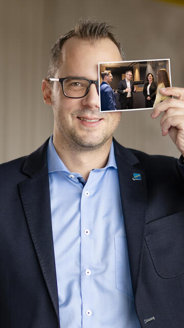 Mann ist Finanzierungsexperte und hält ein Bild wo er Filialleiter ist.